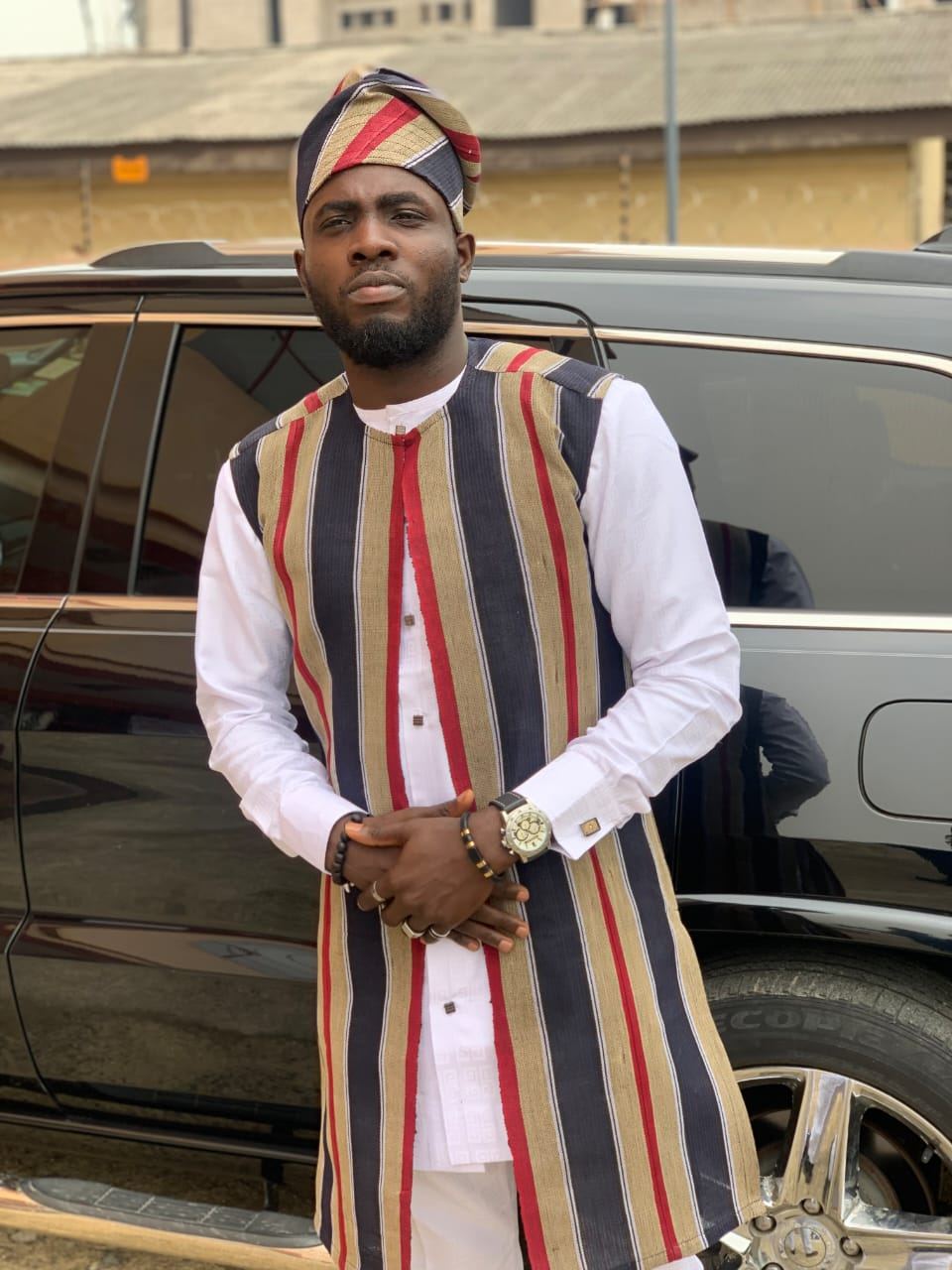 Man standing in a striped aso oke agbada gown and matching cap